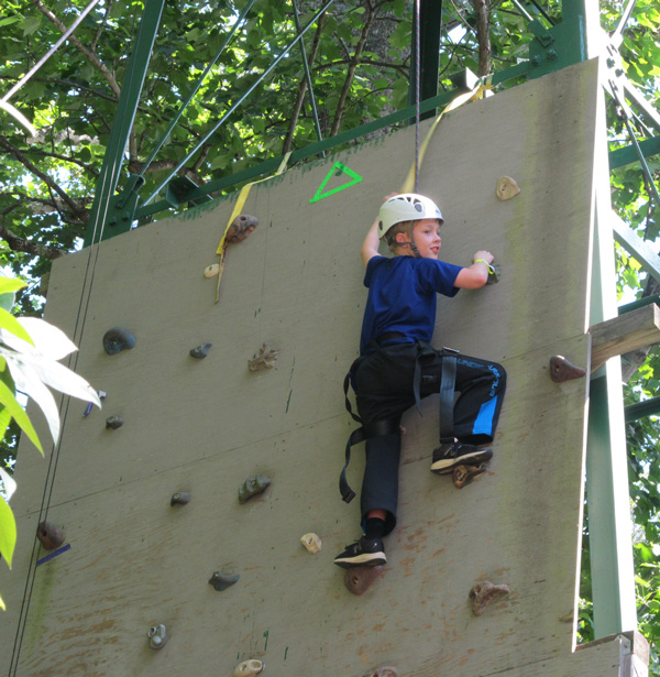Youth climbing the rock wall and ringing the bell at the top.