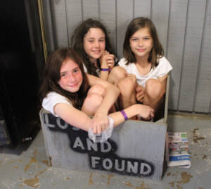 3 girls stuffed themselves into the wooden lost and found box. Smiling at the camera.