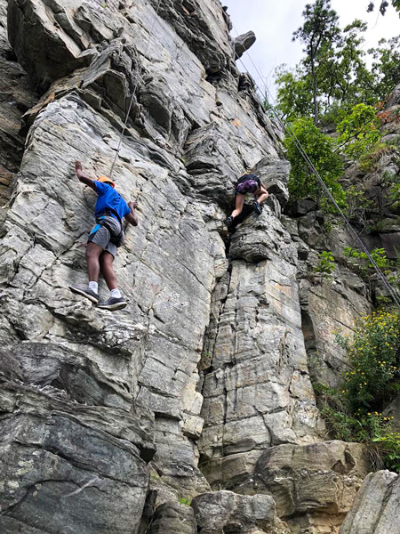 Adventure Trekkers climbing up a rock cliff face with ropes.