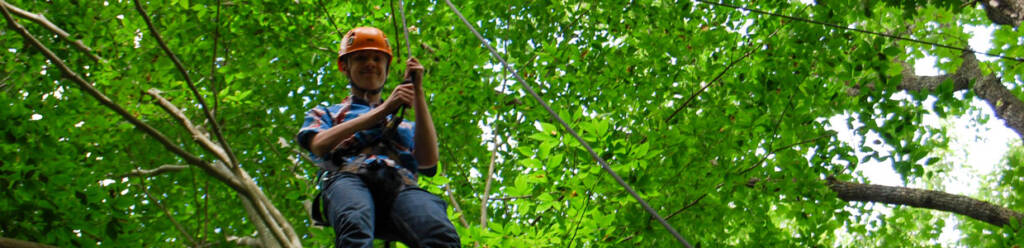 teen up in a tree with safety ropes on for high ropes climbing